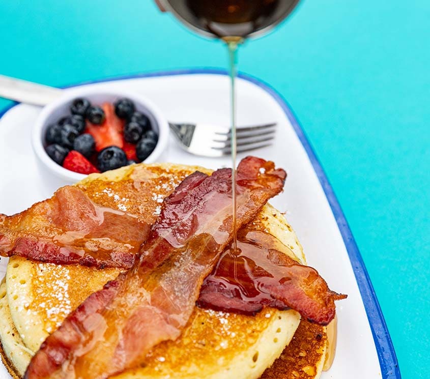 Pancakes, bacon, a side of fruit and drizzling maple syrup, at Biscuit Belly